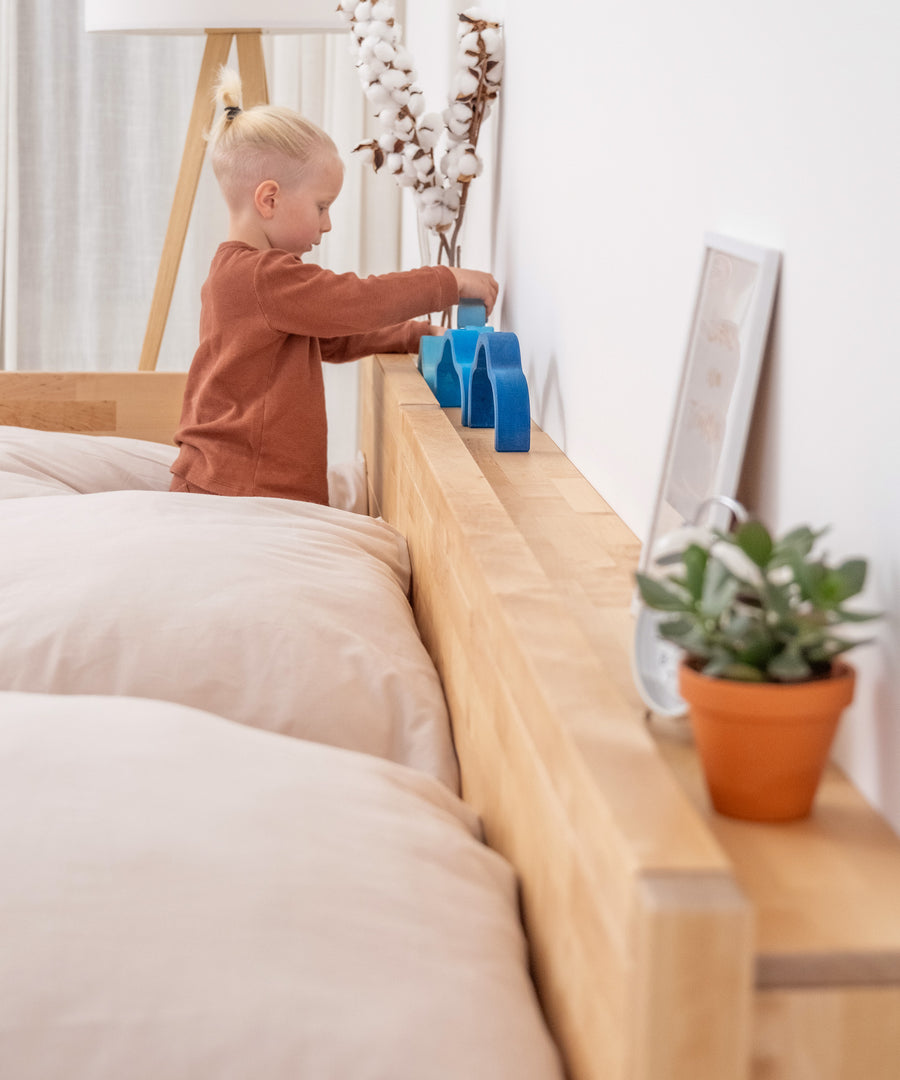 Praktische Ablage*Mit der platzsparenden Ablage im zeitlosen Design hast du alles schnell zur Hand, was du nachts brauchst.|Kind spielt mit Holzspielzeug auf Ablage hinter Bett.