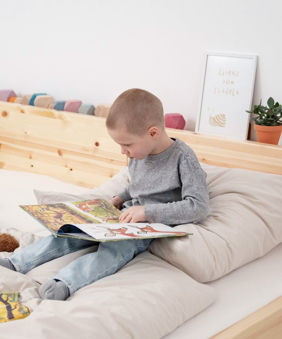 Junge sitzt in Familienbett Kiefer und schaut ein Buch an.