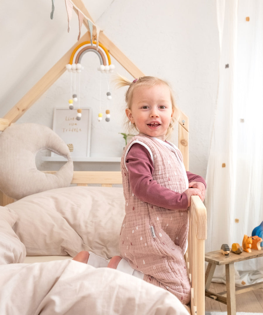 Mädchen in Hausbett Kiefer Natur sitzt neben Rausfallschutz.