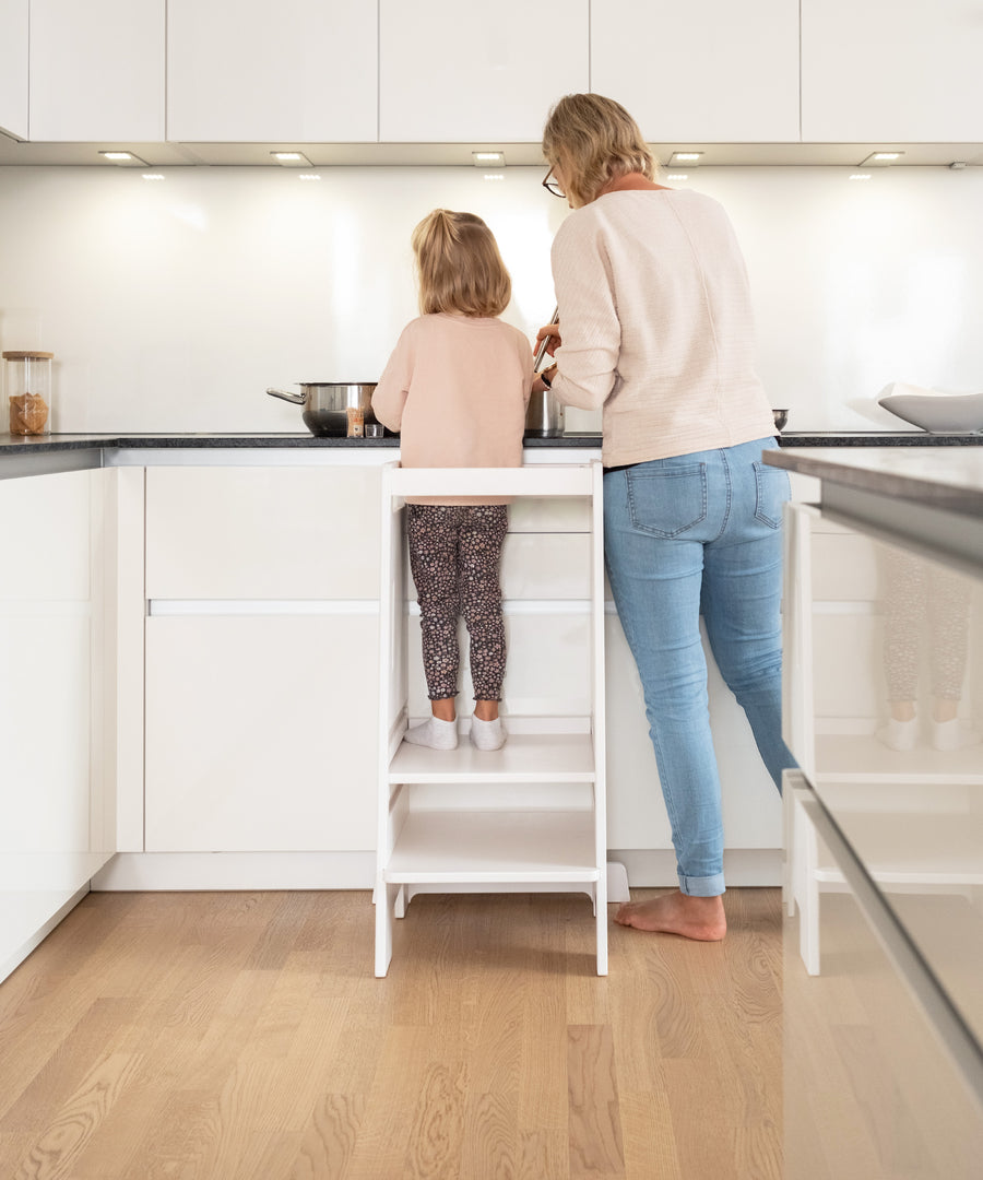 Gemeinsam lernen*Mit dem Lernturm nimmt dein Kind aktiv am Familienalltag teil.
Darin steht es Seite an Seite mit dir und kann spielerisch lernen.|Ein Kind steht auf einem Lernturm und hilft einer Erwachsenen beim Schneiden von Gemüse.