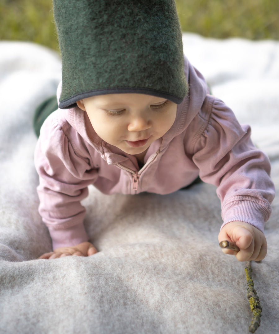 Wärmeregulierend*Die Walkdecke aus Bio-Schurwolle ist wärmeregulierend und schmutz-abweisend. Sie eignet sich perfekt als Outdoor-Krabbeldecke.|Baby krabbelt auf Walkdecke.