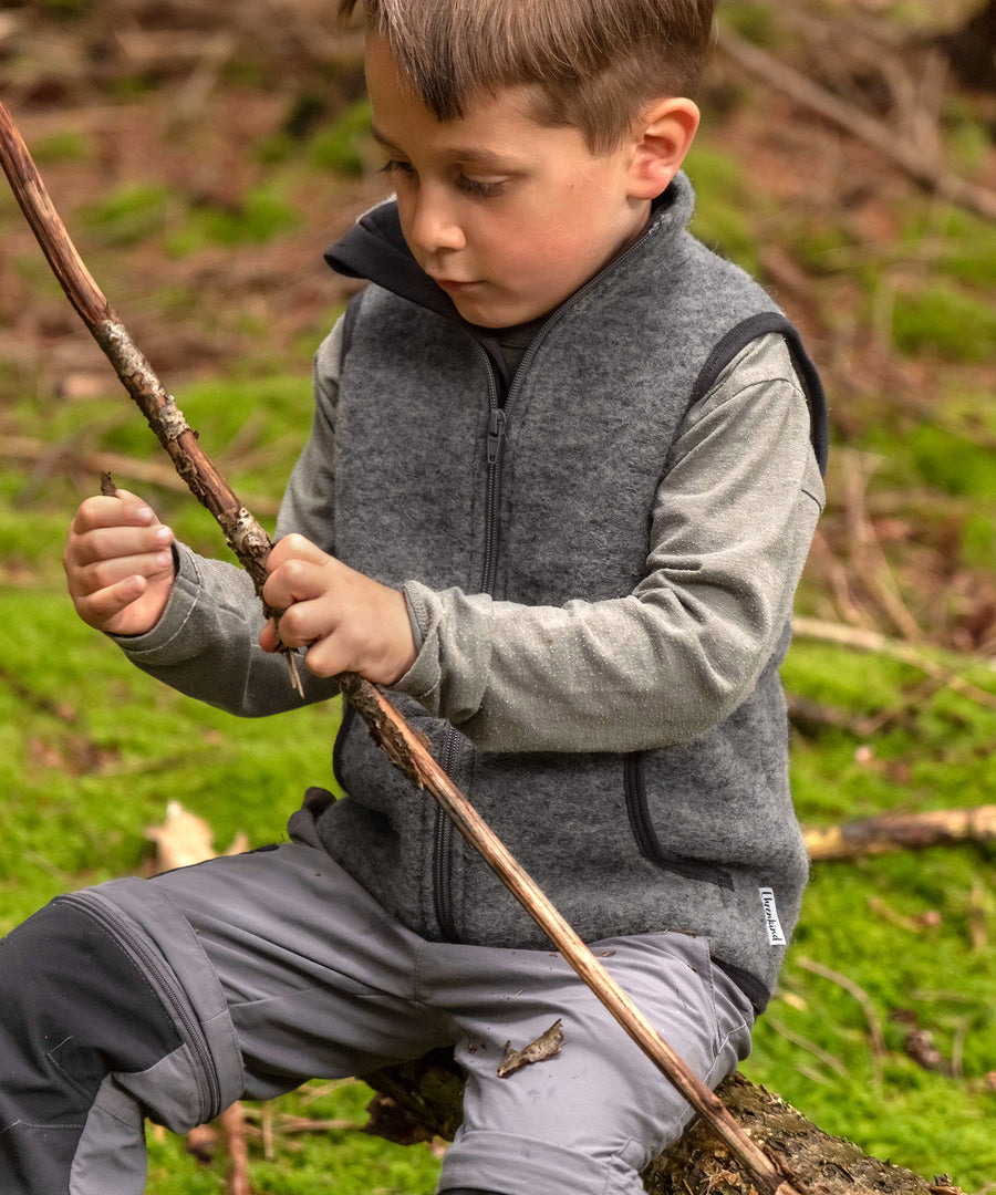 Vielseitig & atmungsaktiv*Wollwalk ist wärmend & temperaturausgleichend. Über dem Pullover oder unter der Jacke - die Weste ist perfekt für den Zwiebellook.|Kind spielt mit Stock im Wald.