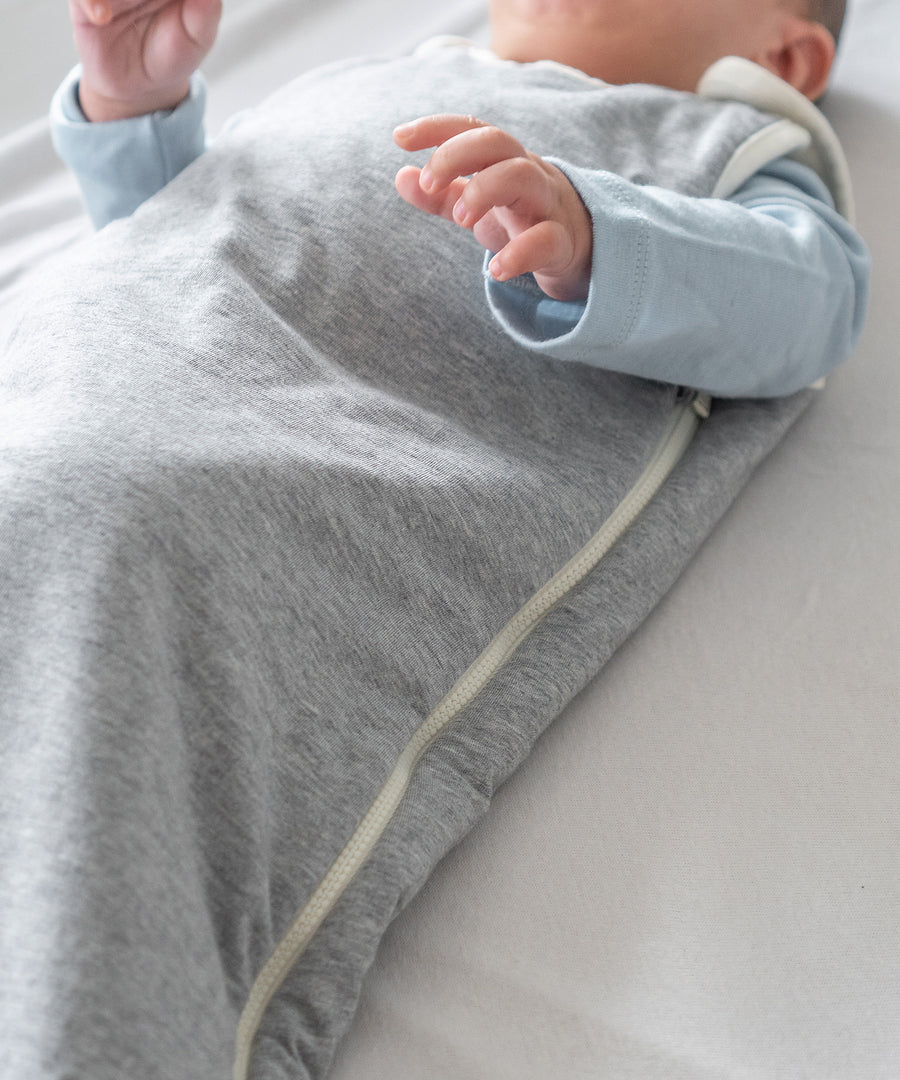 Baby in grauem Schlafsack liegt auf einer Decke.