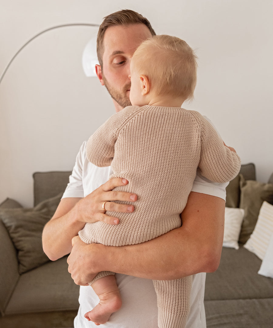 Natürlich sanft zur Babyhaut*Kuschelweicher Strickoverall aus 100% Bio-Baumwolle - atmungsaktiv und sanft zu empfindlicher Babyhaut ab dem ersten Tag.| Vater trägt sein Baby im kuscheligen Strickoverall aus Bio-Baumwolle.
