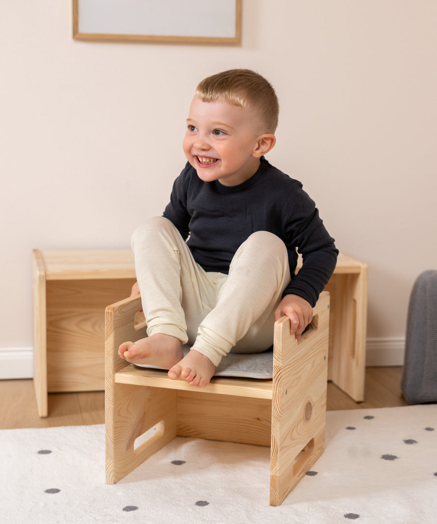 Für zusätzlichen Sitzkomfort*Unser Sitzkissen fügt sich passend in die Sitzfläche ein und macht das Sitzen auf dem Hocker noch angenehmer.| Kind sitzt mit dem Sitzkissen auf dem Hocker Kiefer.