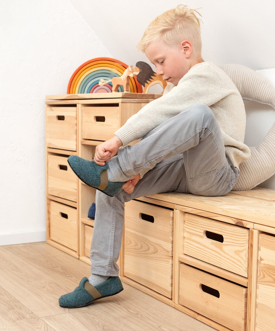 Einfach selbst anzuziehen*Dank Schlupfform mit Gummizug gelingt das Anziehen ganz leicht - ideal für Kinder, um die Selbständigkeit zu fördern.|Junge zieht Kinder-Hausschuhe Flach in Waldgrün an.
