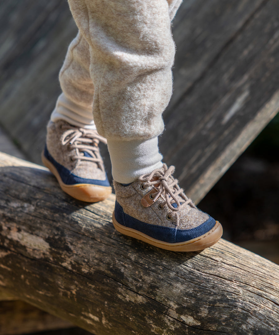 Die ersten Schritte im Freien*Unsere Lauflernschuhe aus Wollfilz begleiten kleine Entdecker warm und bequem durch die kühle Jahreszeit.| Kind trägt die Lauflernschuhe in Dunkelblau beim Klettern.