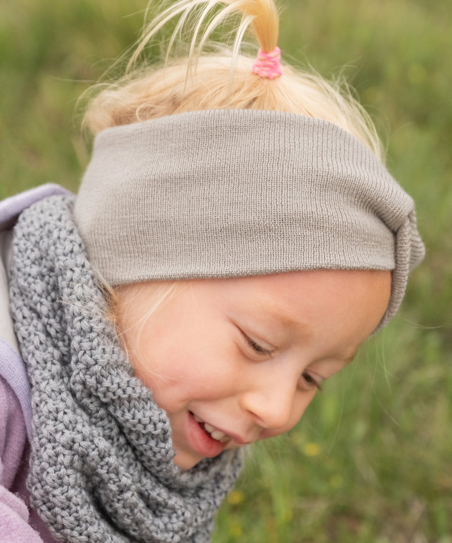 Kind spielt draußen im Herbst mit Knotenstirnband aus elastischer Merinowolle.