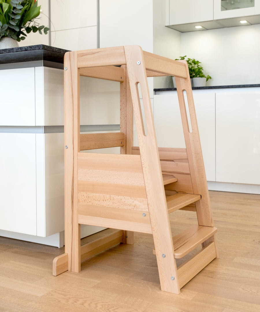Leicht & stabil zugleich*Luftiges Lamellen-Design für alltagstaugliche Handhabung im Familienleben — ca. 5 kg leichter als klassische Modelle.| Buche Natur Lernturm steht an der Kücheninsel.