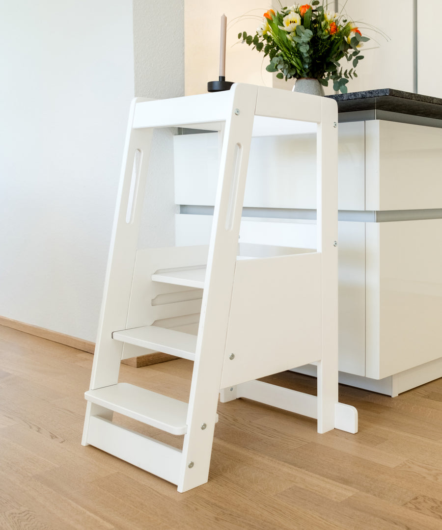 Leicht & stabil zugleich*Luftiges Lamellen-Design für alltagstaugliche Handhabung im Familienleben — ca. 5 kg leichter als klassische Modelle.| Weiß lackierter Lernturm steht an der Kücheninsel.