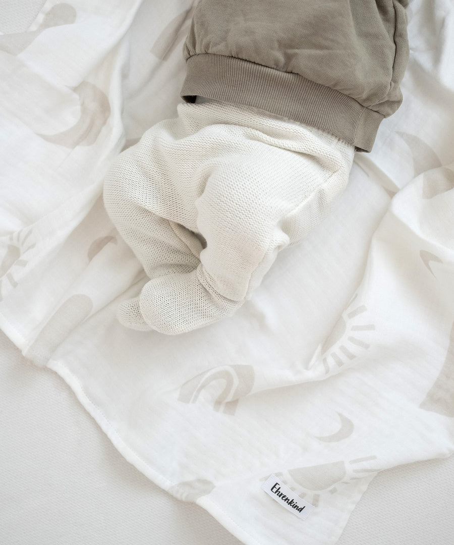 Baby liegt auf Mullwindel aus Farbvariante Beige mit Muster.