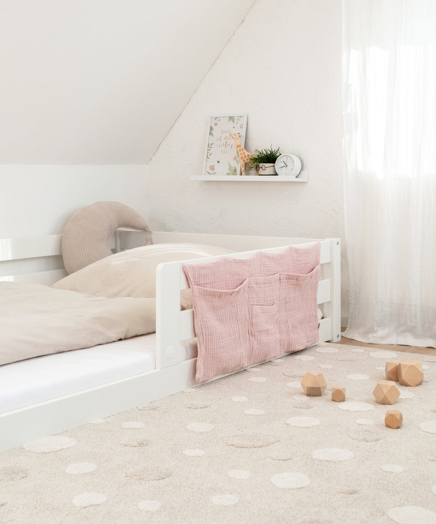 Flexibel einsetzbar*Der Organizer passt an Baby- oder Kinderbetten und kann als Ordnungshilfe überall im Raum einfach angebracht werden.|Bett Organizer in Rosa an einem weißen Kinderbett.