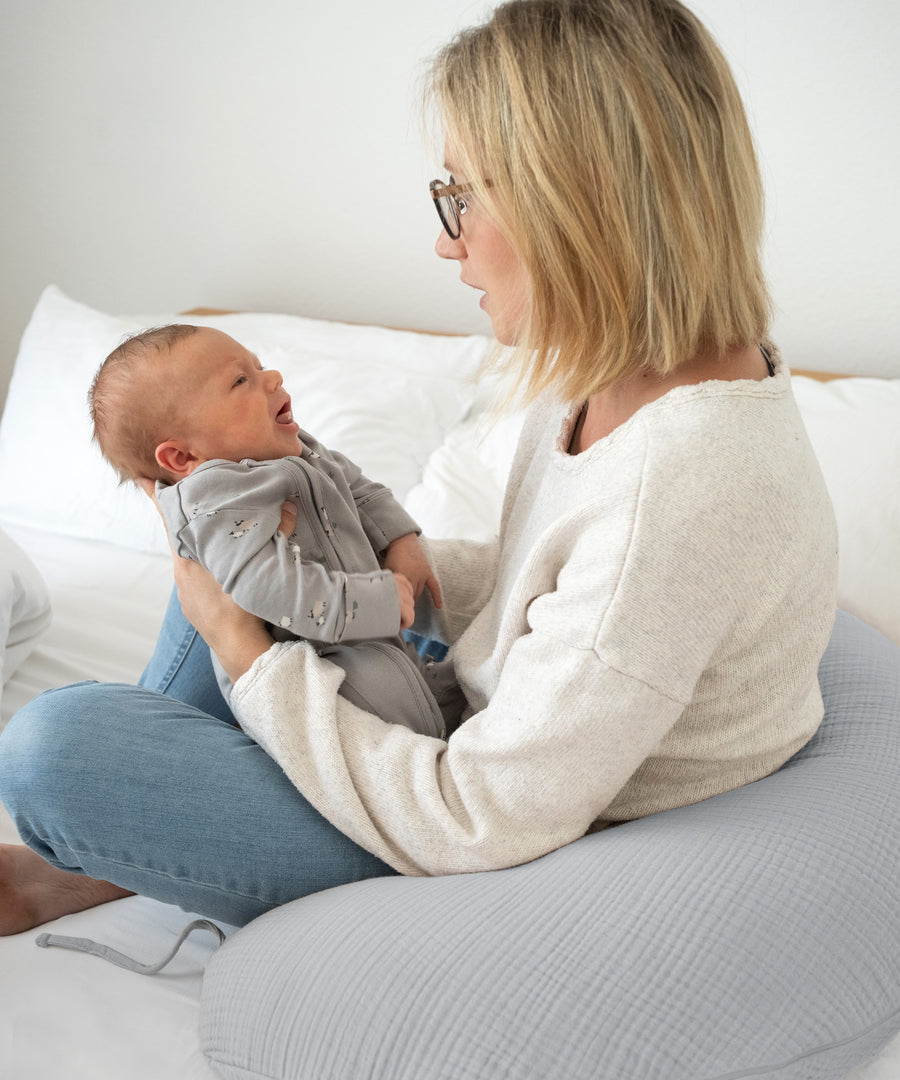 Frau mit Baby an Stillkissen gelehnt.