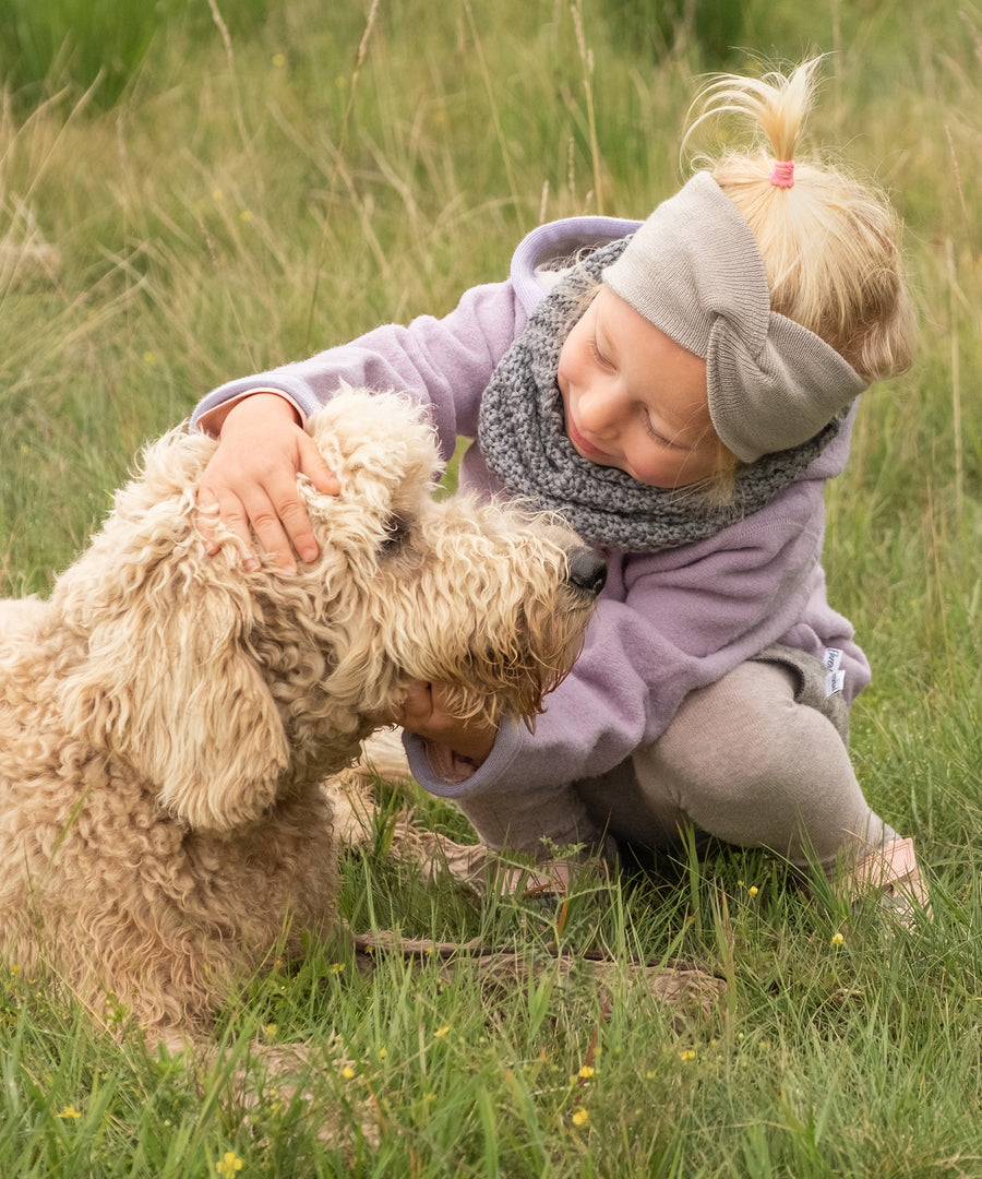 Kind spielt draußen im Herbst mit Hund und trägt Knotenstirnband in Beige.